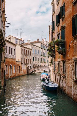 Boats moored at the walls of a building in a canal in Venice, Italy. Classic Venetian street views - wooden shutters, brick houses, bridgesの写真素材