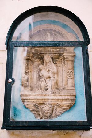 Architectural detail - a bas-relief sculpture of the Virgin Mary with the baby Jesus. Venice, Italy. The bas-relief is decorated with a frame in the form of columns and an arch from aboveの写真素材