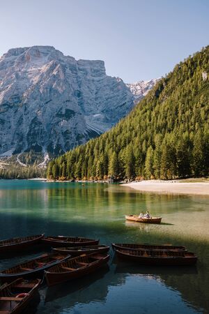 Wedding couple swim in a wooden boat on Lago di Braies in Italy. Newlyweds in Europe, at Braies Lake, in the Dolomites. The groom rows with oars, the bride sits opposite him.の写真素材