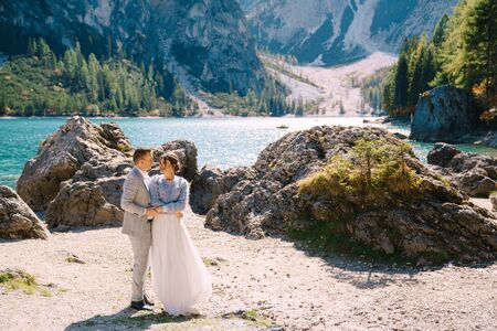 Bride and groom stand against the backdrop of stones overlooking Lago di Braies in Italy. Destination wedding in Europe, on Braies lake. Loving newlyweds walk against the backdrop of amazing nature.の写真素材