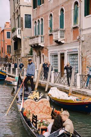 Venice, Italy - 04 october 2019: Italy wedding in Venice. A gondolier rolls a bride and groom in a classic wooden gondola along a narrow Venetian canal. Newlyweds are sitting in a boat and kissing.のeditorial素材