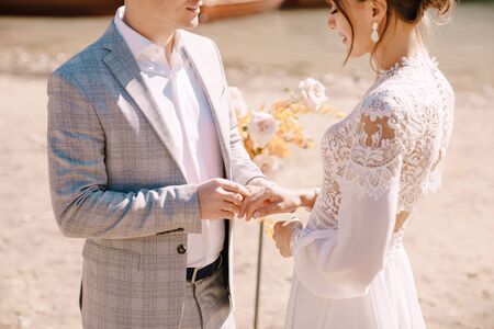 The groom puts on a ring to the bride, at the venue for ceremony, with an arch of autumn flower columns, against the backdrop of Lago di Braies in Italy. Destination wedding in Europe, on Braies lakeの写真素材