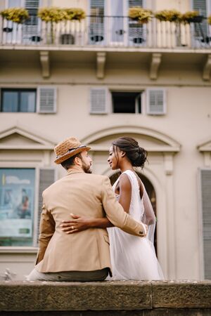 Wedding in Florence, Italy. Multiethnic wedding couple. African-American bride in a white dress with a long veil and a bouquet, and Caucasian groom in a sandy jacket and straw hat.の写真素材