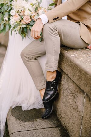Wedding in Florence, Italy. Close-up of the legs of the groom in light short pants and black leather shoes, the bride in a white dress with a bouquet in her hands.の写真素材