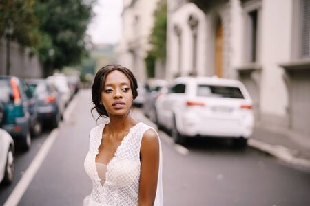 Wedding in Florence, Italy. African-American bride, close-up portrait, in a white dress, with a long veil, walks along the road on a city street.の写真素材