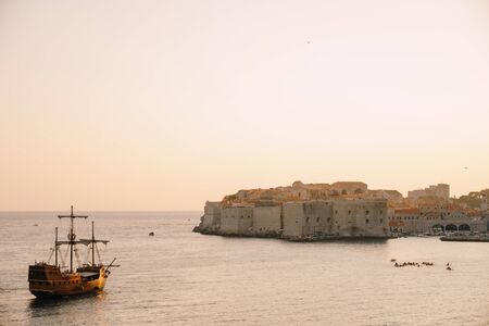The old city of Dubrovnik against the sunset sky. The wooden sailing ship Galleon approaches the main pier of Dubrovnik.の写真素材