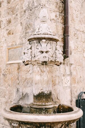Close-up small fountain at the corner of the building, in a square in the old town of Dubrovnik, Croatia. An old drinking stone fountain in the shape of three lion heads.の写真素材