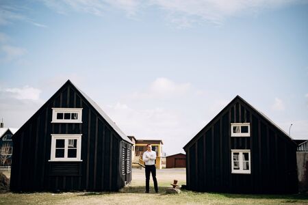 A man in a white shirt between two wooden black houses. Destination Iceland wedding.の写真素材