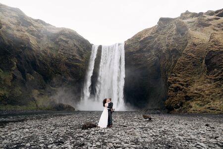 Wedding couple near Skogafoss waterfall. Destination Iceland wedding. The groom kisses the bride.の写真素材