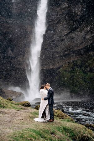 Destination Iceland wedding, near Kvernufoss waterfall. Wedding couple is standing near the waterfall. The groom hugs the bride.の写真素材