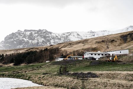 A working construction shop with a hangar, against the background of snow-capped mountains in Iceland. Construction equipment - tractor and excavator.の写真素材