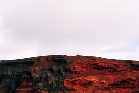 Martian landscapes in Iceland. The red crater of The Seydisholar volcano. The quarry of red soil mining. Silhouette of a man on top of a red-black mountain.の写真素材