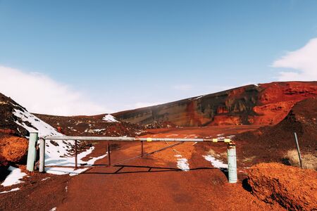 Martian landscapes in Iceland. The red crater of The Seydisholar volcano. The quarry of red soil mining. White snow lies on red soil, Closed gate at the entrance.の写真素材