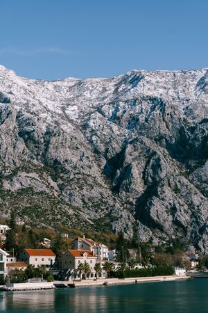 Rocky snow-capped mountains over houses in the Gulf of Kotor, Montenegro.