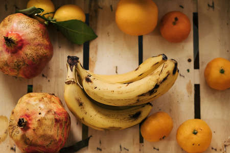 A bunch of bananas in a wooden box surrounded by tangerine, lemons, orange and pomegranates.