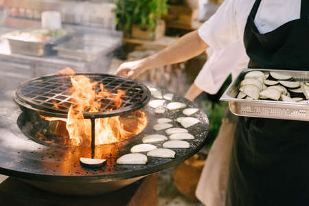 The cook roasts the courgettes. Grilled vegetables. Round bowl-shaped grill with a fire inside.の写真素材