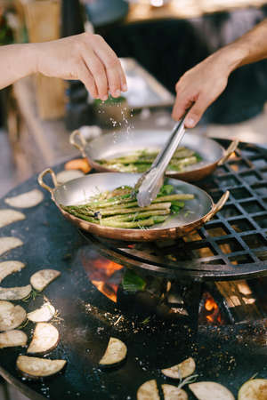 Chefs cook asparagus and eggplant on the grill.