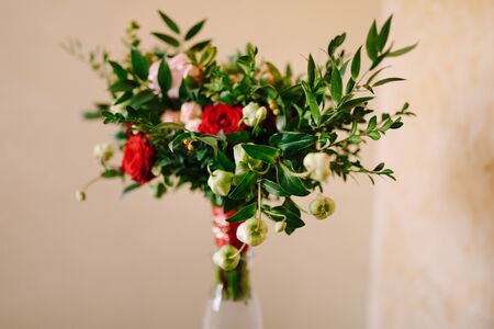 bridal bouquet of red and pink roses, boxwood branches, not blooming buds of white flowers and red ribbons with brooch in the glass vase. High quality photoの写真素材