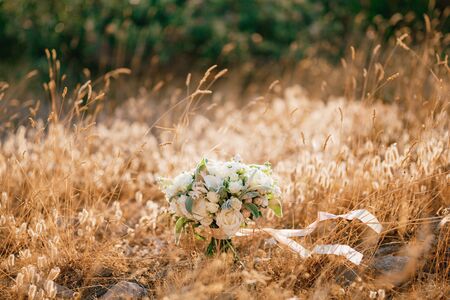 bridal bouquet of white roses, calla lilies, honeysuckle flowers, stachys and white ribbons on the ground in the grassの写真素材