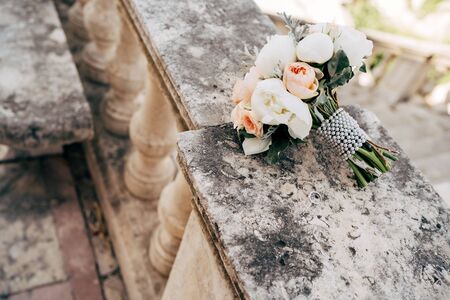 bridal bouquet of white and cream peonies, roses, salal, artemisia with pearl ribbon on the railing of an ancient staircaseの写真素材