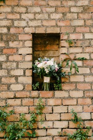 bridal bouquet of pink and white peonies, roses, branches of eucalyptus tree, veronica, matthiola and white ribbons in a niche of a brick wallの写真素材