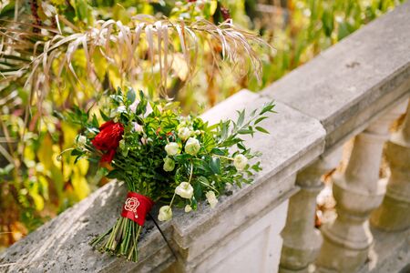 bridal bouquet of red and pink roses, boxwood branches, not blooming buds of white flowers and red ribbons with brooch on the railing of an ancient staircase. High quality photoの写真素材