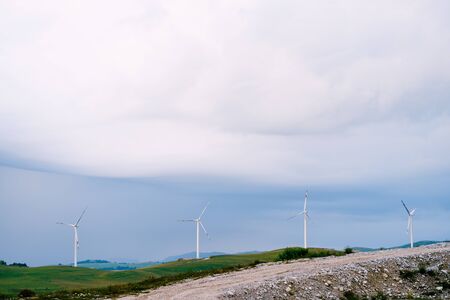 Four large wind turbines stand in a row on the horizon line, against the blue rain clouds.
