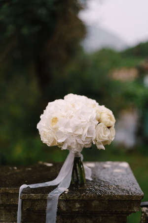 minimalistic bridal bouquet of white roses and hortense with white ribbons on the wet stone railing. High quality photoの写真素材