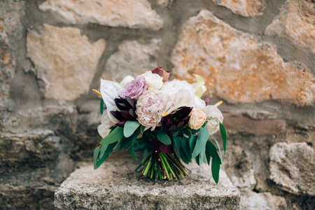 bridal bouquet of white and pink peonies, roses, branches of eucalyptus tree, calla lilies and decorative artichoke on the stoneの写真素材