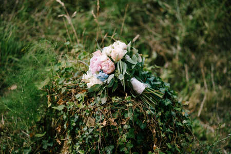 bridal bouquet of white and pink roses, peonies, hortense branches of eucalypt tree, eustoma white ribbons and wedding rings on ivy thicketsの写真素材