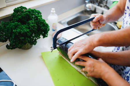 An elderly husband and wife cut a large fish with a saw on the kitchen table.の写真素材