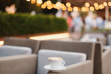 A cup of coffee on a chair in a restaurant with a background on the lights of the garland.の写真素材