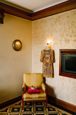 A golden crown encrusted with red and blue gemstones, on a red pillow on a chair in the interior of...