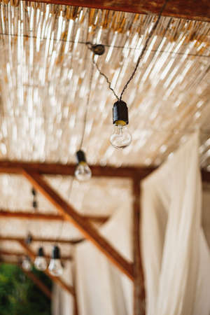 Unpluged garland of incandescent bulbs under the thatched ceiling.の写真素材