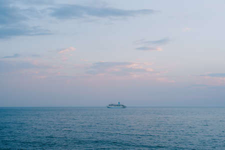 A small cruise liner sails in the open sea against the sunset sky with orange clouds.の写真素材