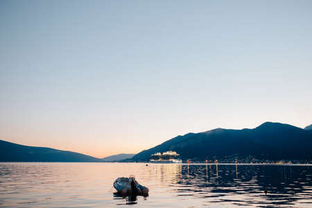The cruise liner sails through Kotor Bay at night, against the backdrop of the mountains. Rubber motorboat in the foreground in the water.の写真素材