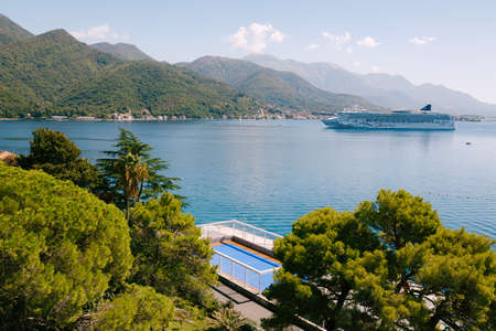 The cruise liner sails into the Bay of Kotor against the backdrop of the mountains above the town of...