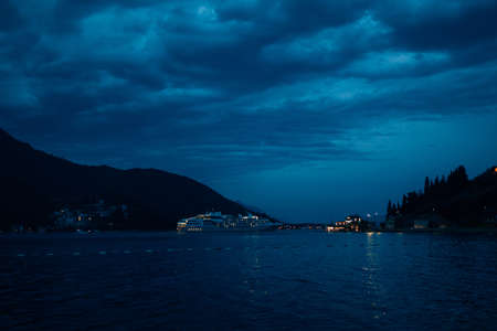 Cruise liner at night, against the backdrop of mountains and cloudy sky with clouds.の写真素材