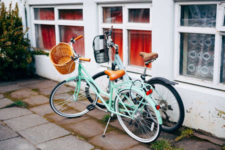 Two bicycles with grocery baskets by an old house with large windows.の写真素材