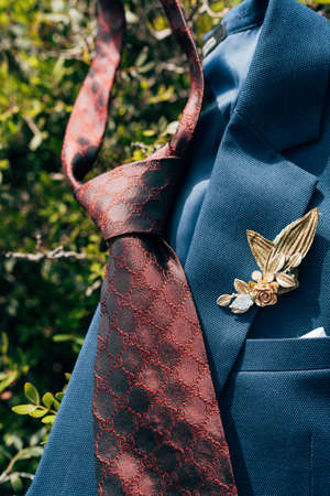 A dark red tie and a blue jacket with a boutonniere on green leaves.の写真素材
