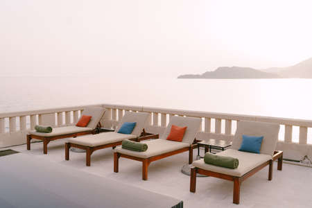 Wooden loungers near the pool at the villa by the sea, at sunset.
