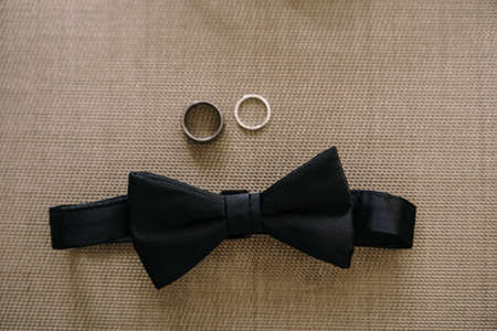 Close-up of a black bow tie and two wedding rings on a gray background.の写真素材