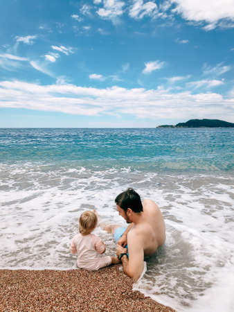 Dad and daughter lie in the sea waves, on a sandy beach in Montenegro, in the Adriatic Sea.の写真素材