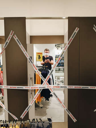 Budva, Montenegro - 01 august 2020: Man wearing a medical mask takes a selfie in the mirror of a dressing room at a NewYorker clothing store, covered with ribbons due to the 2020 coronavirus pandemic.のeditorial素材