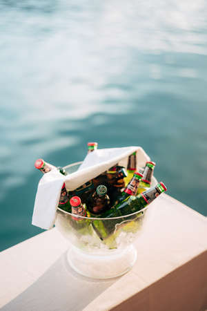 Perast, Montenegro - 03 august 2020: A clear ice bucket filled with bottles of light and dark beers and a white napkin on top on a smooth surface by blue water.のeditorial素材