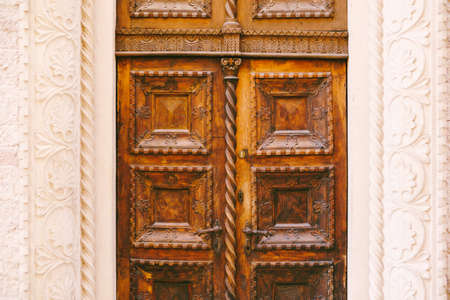 A close-up of brown doors with raised carvings and patterns in a white molded opening.