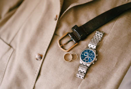 Mens belt, wrist watch and wedding rings on a mens beige jacket.の写真素材
