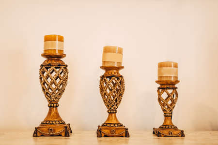 Three openwork candlesticks of different sizes, with beige candles in a row on a light backgroundの写真素材