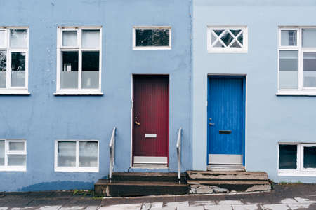 A two-tone building in blue and light blue with two rectangular doors in blue and burgundy and windows of different sizes.の写真素材