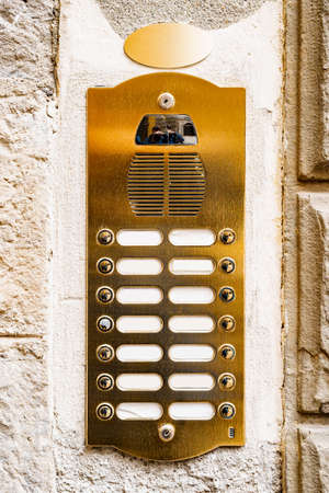 The intercom is golden, metal with buttons and blank columns for apartment numbers on a stone wall.